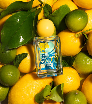 Perfume bottle with leaf design surrounded by lemons and limes
