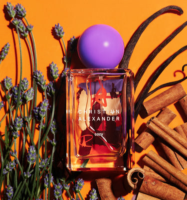Perfume bottle with lavender, cinnamon sticks, and vanilla beans on an orange background
