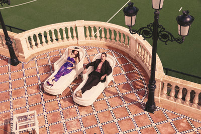 Two people lounging on a tiled patio with decorative lamps, yawning in the sun for a perfume photo shoot