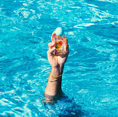 Hand holding a perfumebottle in a swimmingpool