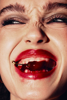 Close-up of a person with red lipstick and biting a cherry.