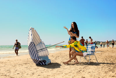 Couple on a beach with a striped parasol holding a perfume bottle in the hand