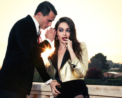 Man and woman in formal attire sitting on a bench with a scenic background